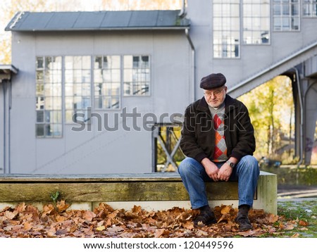Old man sitting on bench, thinking, abandoned railroad station on background