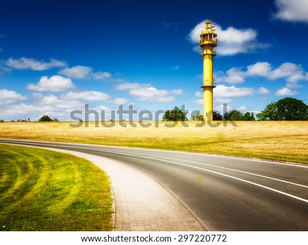 North sea landscape with road and yellow lighthouse on the dike. Friesland, Germany travel destination