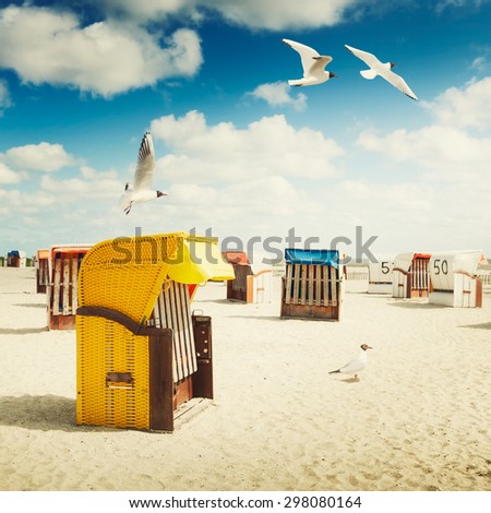 Hooded chairs on sand beach. Sea gulls flying in blue cloudy sky. Vacation background. North sea coast, travel destination. Toned in warm colors