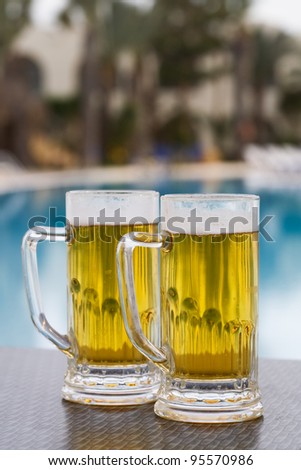 Two beer mugs by swimming pool in tropical resort
