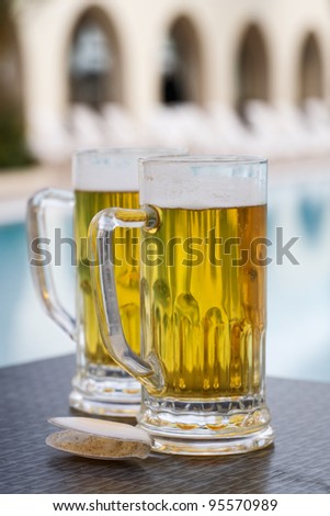 Two beer mugs and shell by swimming pool in tropical resort