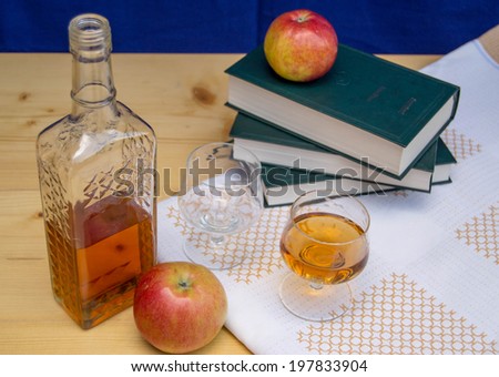 Glass and bottle of hard liquor like scotch, bourbon, whiskey or brandy on wood background with books and apples on white texture