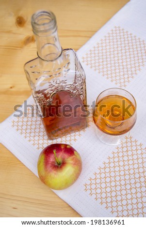 Glass and bottle of hard liquor like scotch, bourbon, whiskey or brandy on wood background and white texture and an apple
