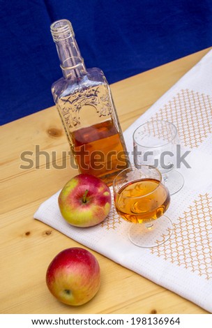 Glass and bottle of hard liquor like scotch, bourbon, whiskey or brandy on wood background and white texture and two apples