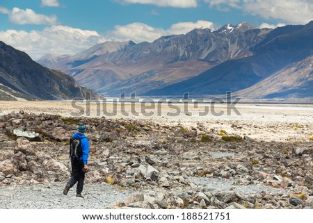 A man enjoys the view of the glacier and the lake from Glentanner Park Centre near Mount Cook, on a background of blue sky with clouds, snowy Southern Alps in New Zealand.