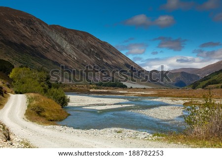 Amazing mountains and river water near a gravel road winding through the pass going to Queenstown in New Zealand.