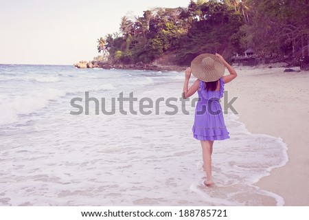 Woman running on the beach wearing a straw hat and a blue short dress. Vacation. vintage.
