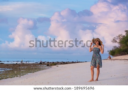 young girl in a straw hat and beach dress walks along the coast at dawn. Background blue sky with beautiful clouds, clouds.