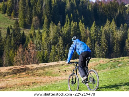 mountain biker on sunny give rides on the rolling hills of green forest