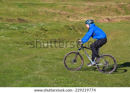 mountain biker on sunny give rides on the rolling hills of green forest against the blue sky with beautiful clouds
