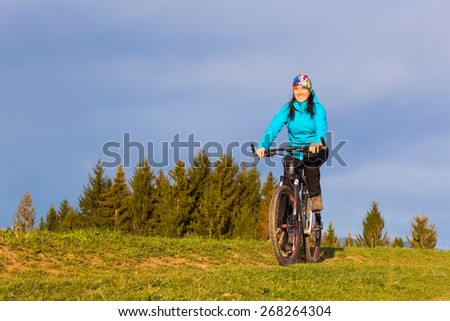 mountain biker on sunny day riding on a winding dirt road in a rural hilly area of green forest against the blue sky with beautiful clouds