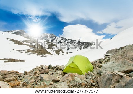 Tent stands in extreme conditions on the rocks. Background blue sky and mountain peaks in the snow.