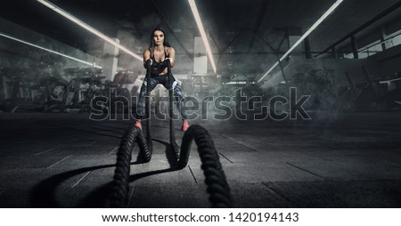 Sport. Battle ropes session. Attractive young fit sportswoman working out in functional training gym doing exercise with battle ropes.