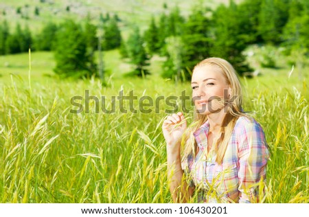 Cute blond girl on wheat field, woman sitting on green grass, female relaxing outdoor, happy pretty teen girl holding rye, young lady enjoying nature, summer rural vacation, peaceful calm person