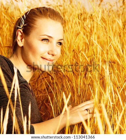 Photo of attractive smiling girl sitting in golden wheat field, closeup portrait of beautiful young blond female on yellow hay ryes background, grain harvest season, conceptual of autumn season