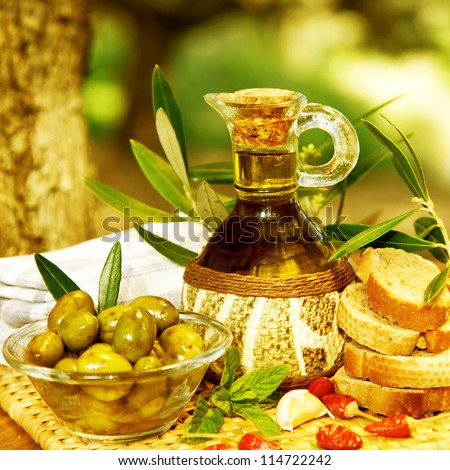 Photo of olive oil still life, healthy organic salad dressing, lebanese cuisine, glass bottle with olive oil, marinated olives and bread on tray in garden, homemade food, harvest season