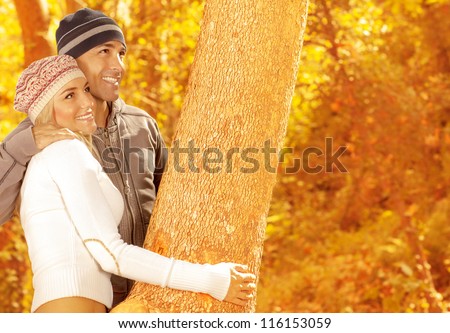 Photo of of happy couple playing game in autumn park, closeup portrait of two loving people hugging tree, cute woman and handsome guy wearing stylish warm hats, happiness and affection concept