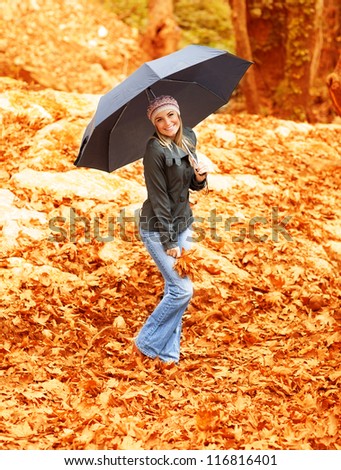 Picture of attractive woman walking under umbrella in rainy day in autumnal park