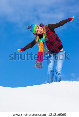 Image of pretty playful female having fun in winter park, cute woman standing with raised up hands on the top of snowy mountain, colorful hat and scarf, wintertime holidays, freedom concept