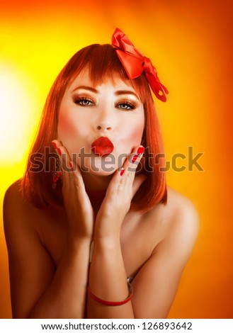 Photo of pretty redhead woman with beautiful red bow in hair isolated on yellow background, closeup portrait of attractive female with stylish makeup make kiss, Valentine day, love concept