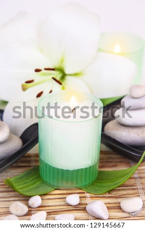 Picture of pebble stones in black bowl, white lily flower, fresh green leaves, candle on wooden table in spa salon, holiday and vacation in luxury spa resort, herbal massage, alternative medicine