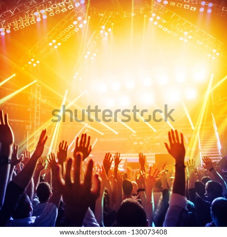 Picture of a lot of people enjoying night perfomance of famous dj, large crowd of youth dancing with raised up hands on rock concert, party in dance club, bright yellow light from stage, nightlife