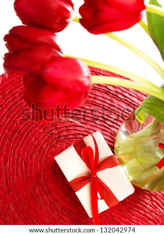 Beautiful fresh red tulips bouquet in glass vase and little white gift box decorated with ribbon on the table, romantic present
