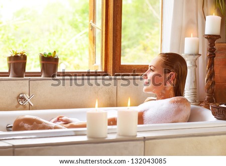 Beautiful woman taking bath at home, cute female lying down in bathtub, warm candle light, romantic atmosphere, pampering and hygiene, spa resort in hotel, zen balance concept