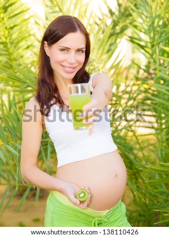 Beautiful pregnant female having breakfast outdoors, drink tasty kiwi juice, eat fresh fruits, healthy pregnancy, new life concept