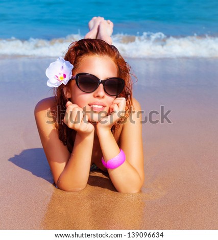 Closeup portrait of beautiful female with fresh orchid flower in red hair lying down on the beach, luxury spa resort, summer traveling and vacation concept