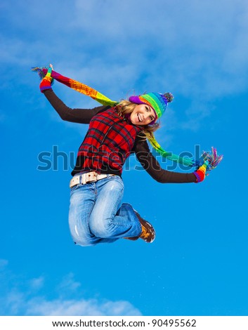 Happy girl jumping over blue sky background, teen outdoor winter activities, female having fun at Christmastime, woman wearing colorful clothes, freedom and success concept