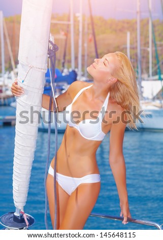 Sexy blond woman tanning on the sailboat, attractive girl enjoying bright sun shine in yacht port, summer vacation concept