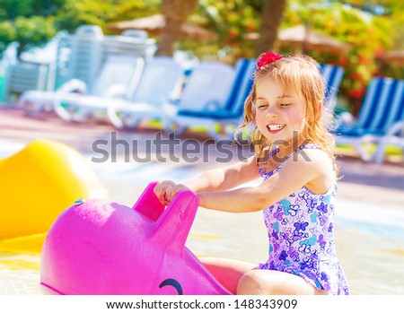 Happy baby girl having fun in aquapark, swimming in the pool on pink inflatable toy, daycare in summertime