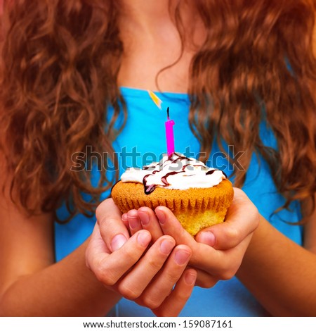 Celebrating birthday of teen girl, holding in hands tasty cupcake with one candle, make a wish, body part, brown curly hair, holiday concept