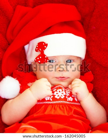 Portrait of cute baby girl wearing red Santa Claus hat with bow lying down in the bed at home, New Year party for children