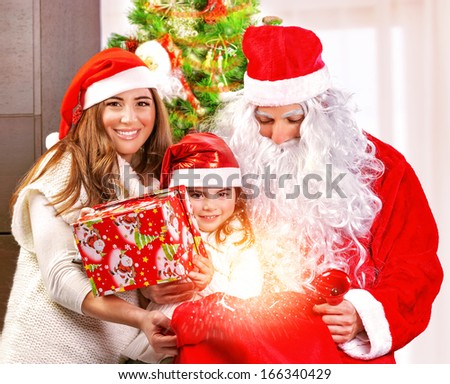 Happy Christmas celebration, cheerful parents give festive gift to adorable sweet child, wearing Santa Claus costume, New Year party concept
