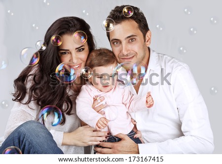 Portrait of cute arabic baby girl with mother and father playing with soap bubbles, enjoying family, love and happiness concept