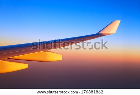 Airplane wings in sunset light, bright orange sun shine, luxury air transportation, business trip, travel and tourism concept