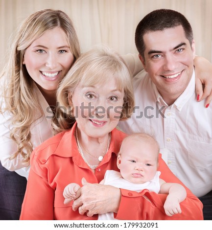 Family generation portrait, beautiful elegant grand mother holding on hands newborn granddaughter, mother and father standing behind them