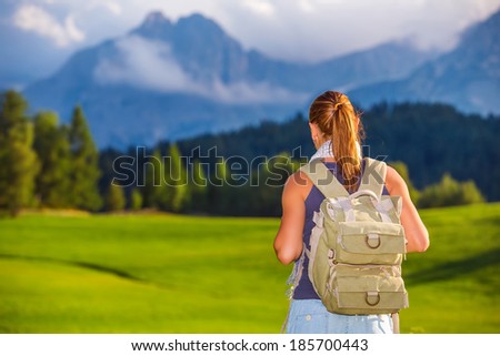 Traveler girl in the mountains, rear view of woman with backpack looking on beautiful landscape, travel to Alps, summer adventure