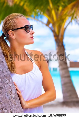 Portrait of attractive female wearing stylish sunglasses hug palm tree trunk, luxury summer vacation, travel and tourism concept