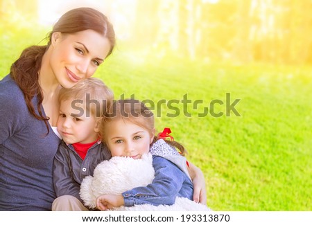 Portrait of beautiful young mother with cute daughter and son sitting on the meadow, sunny day, love and happy family concept