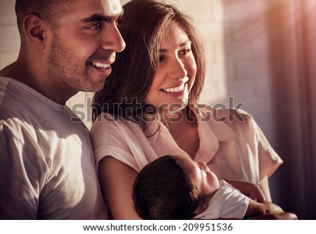 Closeup portrait of beautiful arabic family at home in sunset light, happy parents holding on hands cute little daughter, happiness and love concept