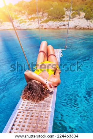 Sexy woman tanning on sailboat, female relaxing above transparent blue sea, girl enjoying bright sun light, active lifestyle, happy summer vacation