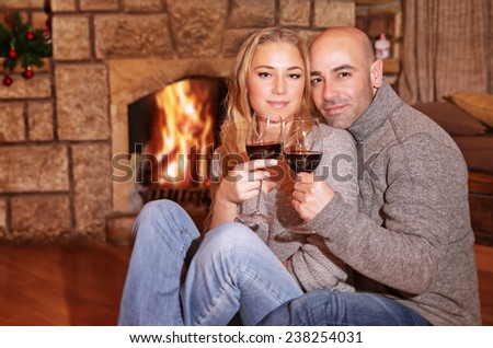 Cute couple on romantic date, beautiful woman with handsome man sitting near fireplace and drinking wine, celebrating Christmas holidays