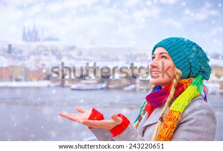 Portrait of cute happy woman enjoy snowfall in beautiful Prague city, catches snowflakes by hands with pleasure, enjoying winter holidays