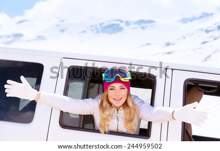 Portrait of cute cheerful woman with raised hands leaned out of the car window, goes to ski, enjoying winter vacation