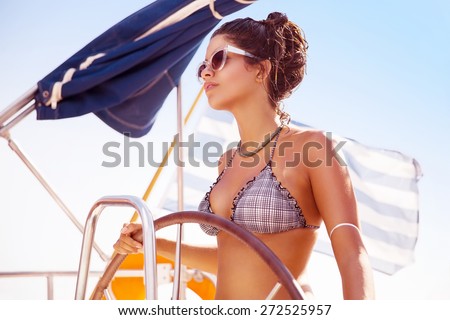 Portrait of beautiful sexy woman behind wheel of luxury sailboat, serious captain driving water transport, enjoying active summer vacation