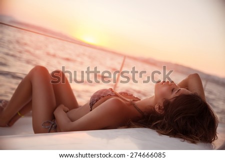 Sexy woman on sailboat lying down on the deck of luxury sailboat, tanning on mild sunset light, enjoying sea cruise, fashion and summer holidays concept