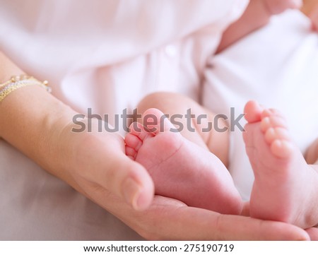 Mother hand holding cute tiny baby feet, doing massage for little newborn child, happy motherhood, protection and safety concept